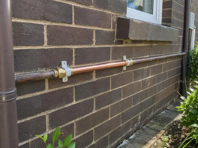 Repaired copper water pipe fixed along a brick exterior wall beneath a window in Lilyfield