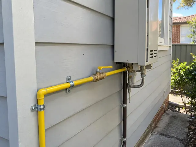 Yellow gas pipe and fittings beside an outdoor wall-mounted unit on a weatherboard house in Haberfield