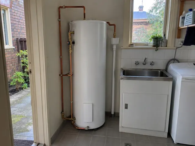 White hot water cylinder beside a laundry sink and tiled wall in a home interior in Rozelle